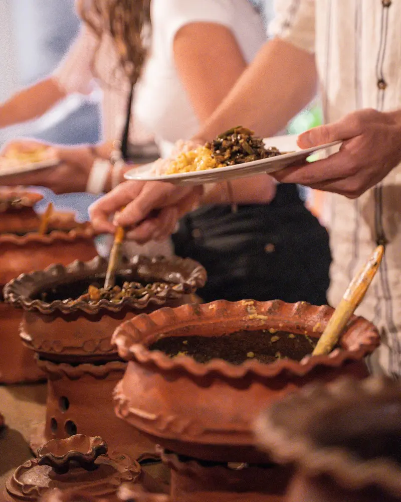 Guests holding out plates as rice and curry is served from clay pots