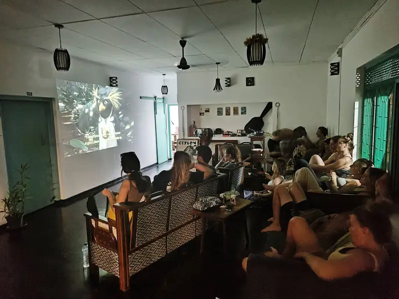 Guests on sofas watching a film projected on the wall of the Weligama common room