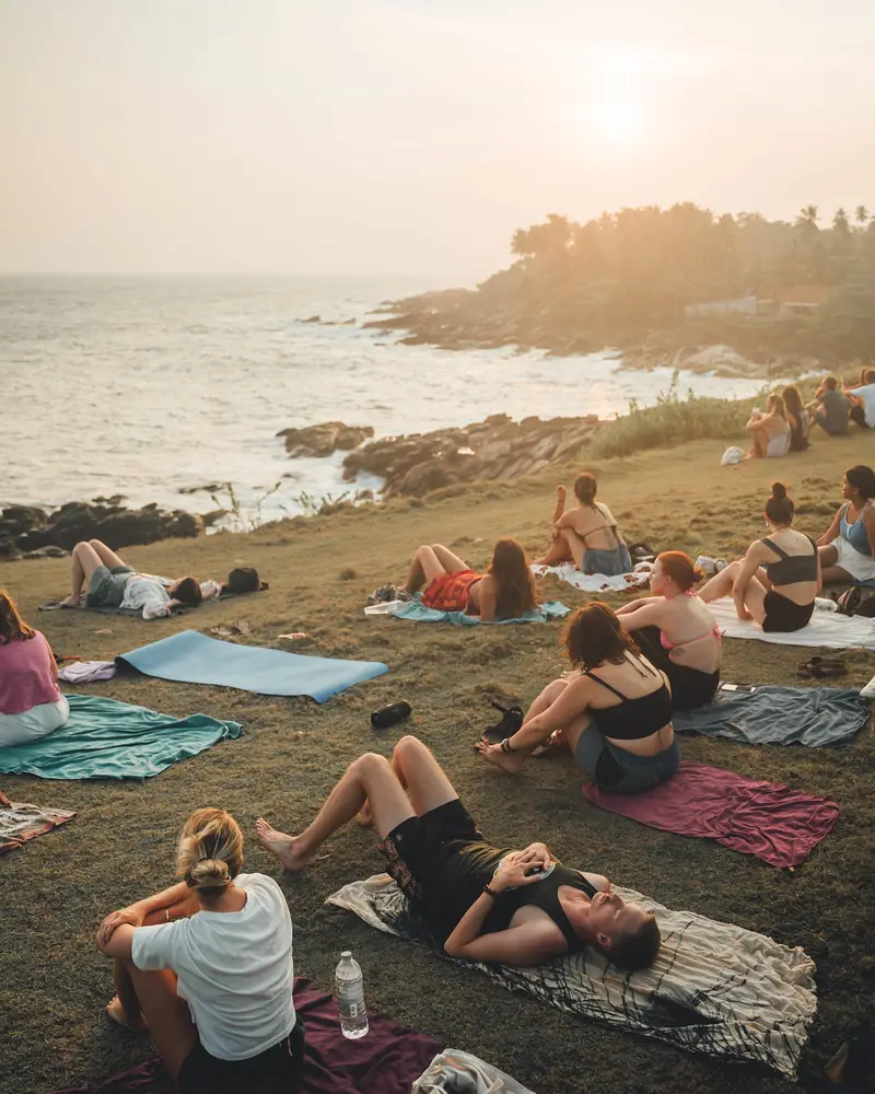 Guests lying on towels on a grassy headland above the sea as the sun goes down
