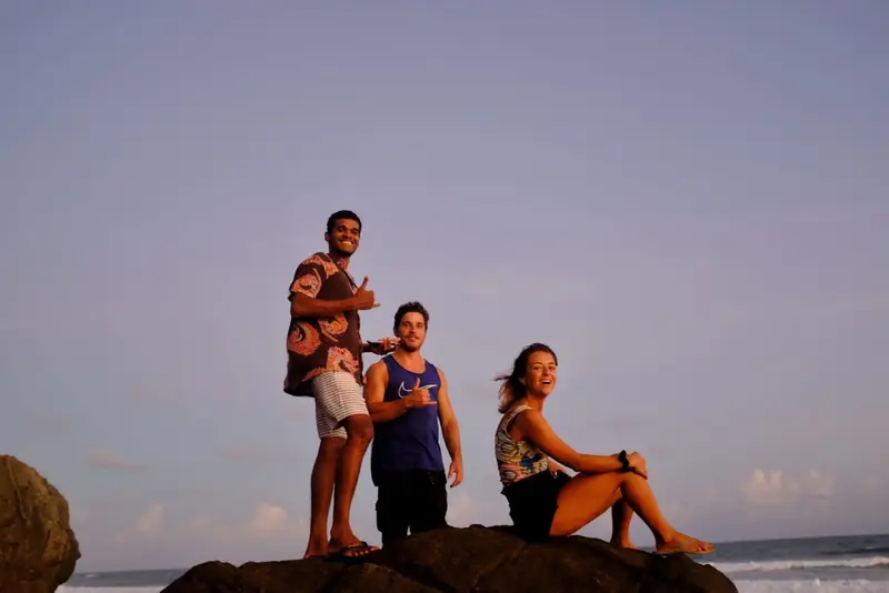 Three guests standing on a rock by the sea at dusk