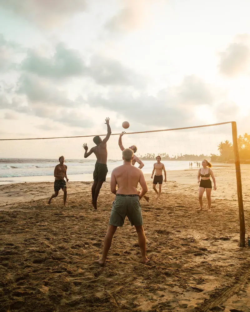 Guests jumping for the ball in a game of beach volleyball in the late afternoon