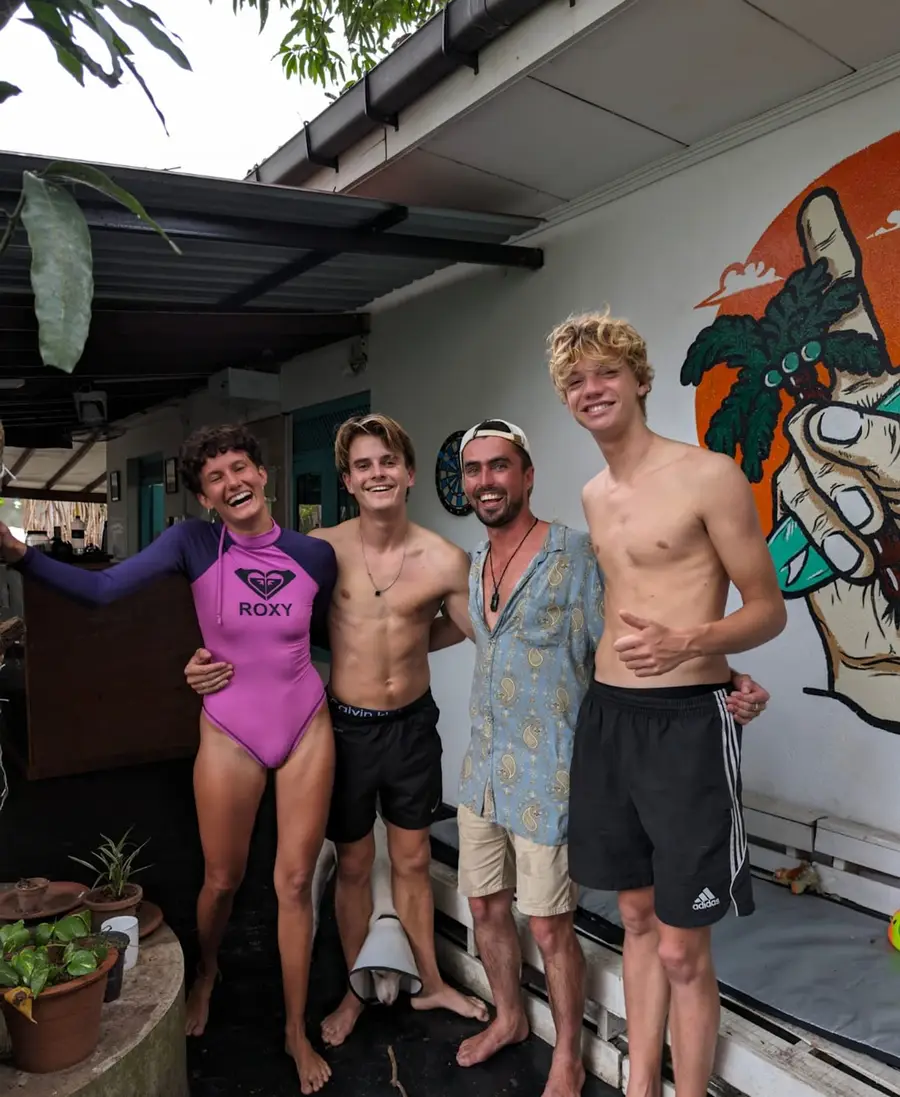 Four guests in wetsuits and board shorts grinning outside the Weligama house after a surf