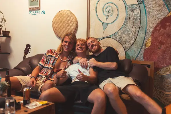 Three guests hugging on the common-room sofa, a guitar propped behind them