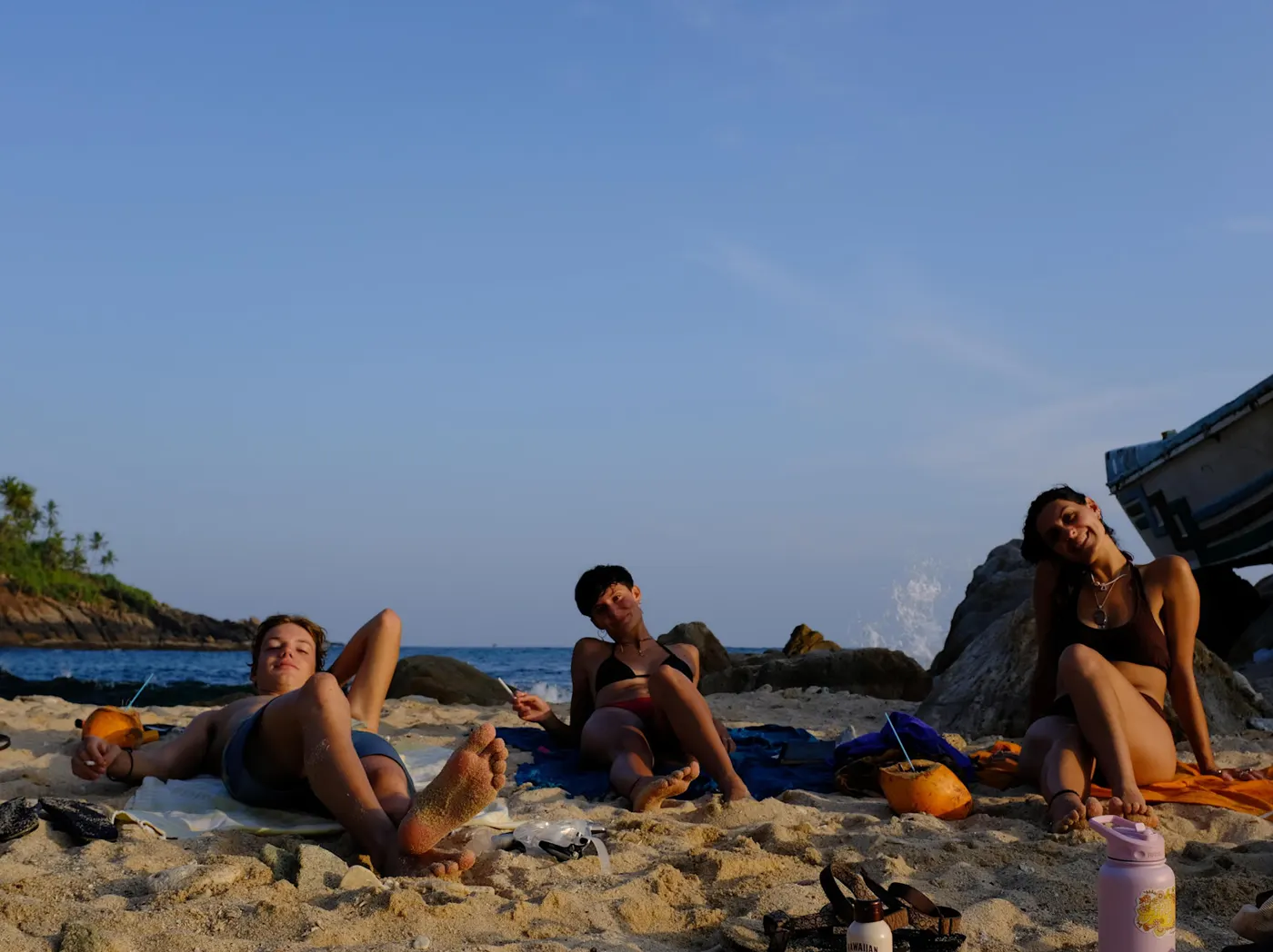 Three guests lying back on the sand by the rocks as the sun goes down