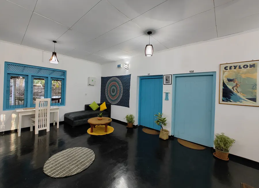 A bright lounge with blue doors, a sofa and a vintage Ceylon surf poster