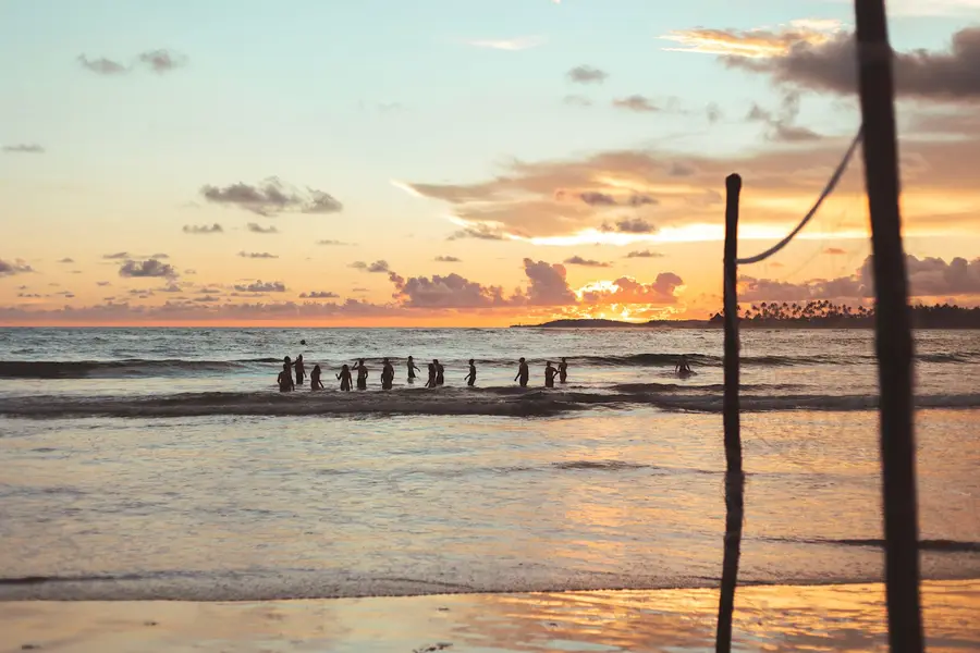 Guests wading into the sea at Hiriketiya at sunset, framed by a wooden post
