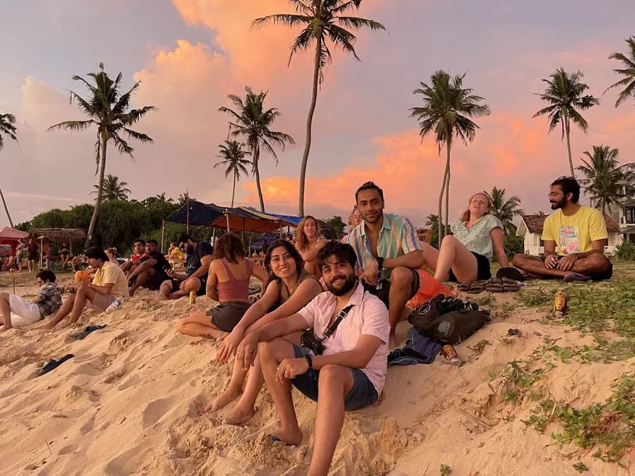 A group of guests sitting on the sand at Weligama beach under palm trees at sunset