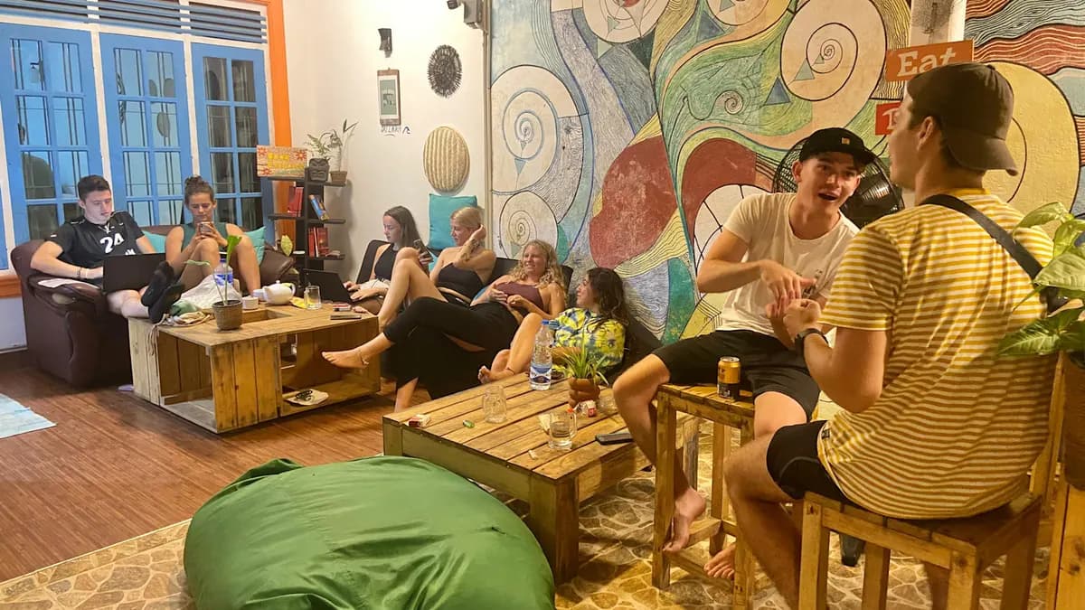 Guests on sofas and stools in the Hiriketiya common room, in front of a swirling painted mural