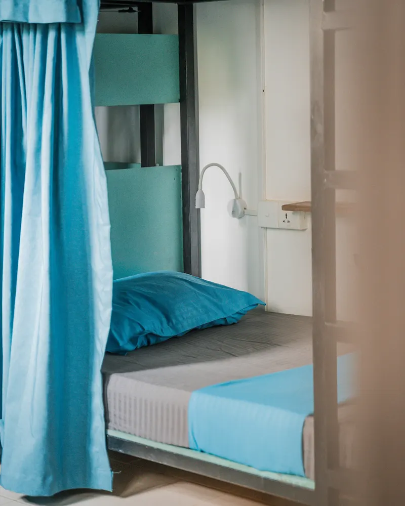 A Hiriketiya bunk with a turquoise curtain, a reading light, a socket and a small shelf