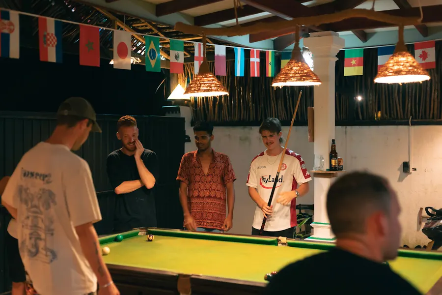 Guests gathered round the pool table at night under strings of flags
