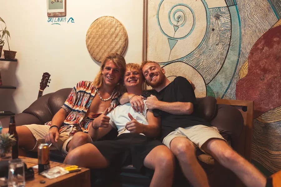 Three guests squeezed onto a leather sofa, laughing, in front of the mural